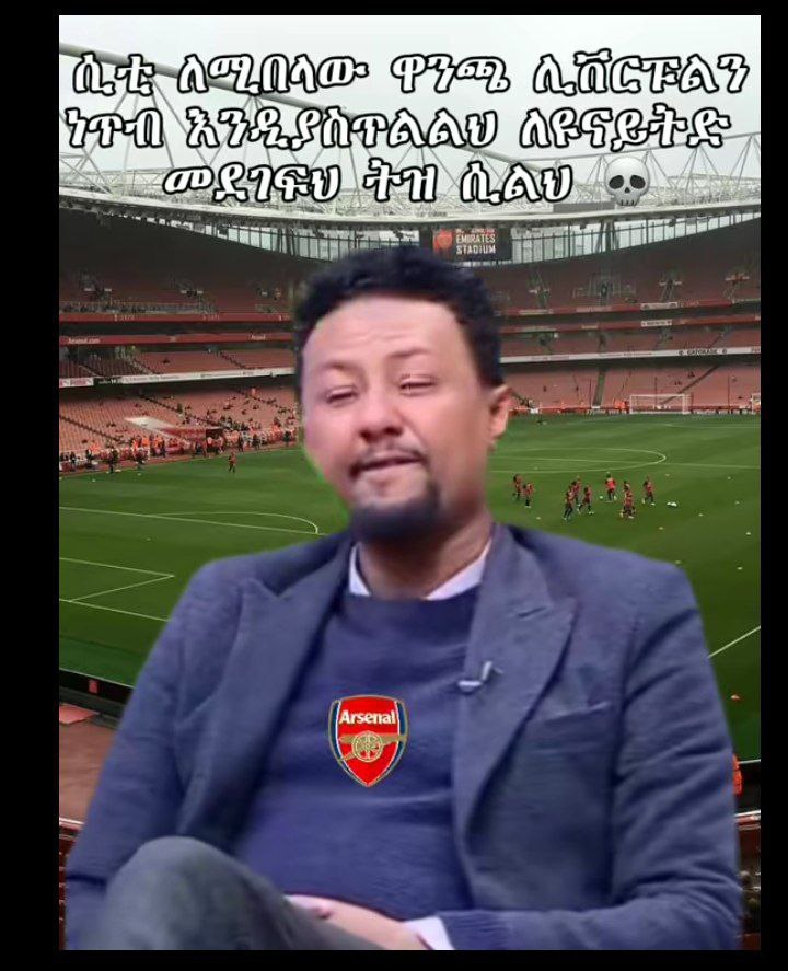 a man in a suit sitting on a chair in front of a soccer field