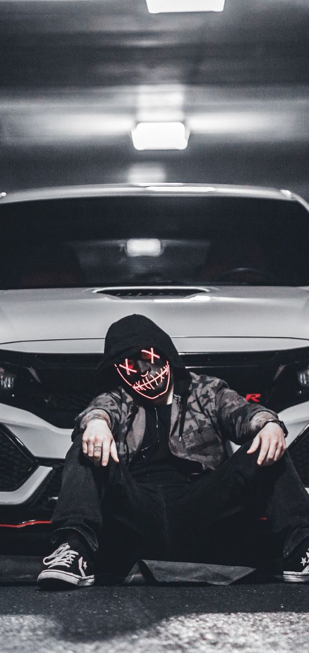 a man in a hoodie sitting on the ground next to a car